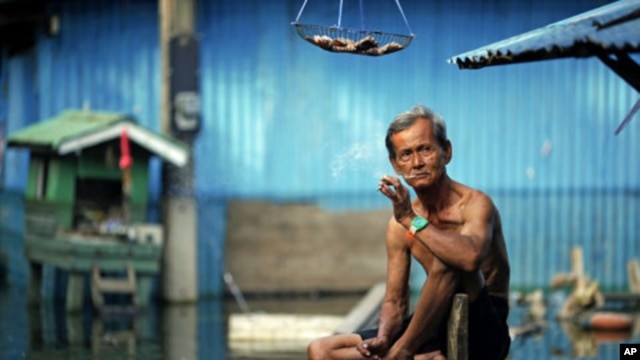 A man smokes a cigarette outside his flooded home in a slum just outside Bangkok, Thailand, November 21, 2011.