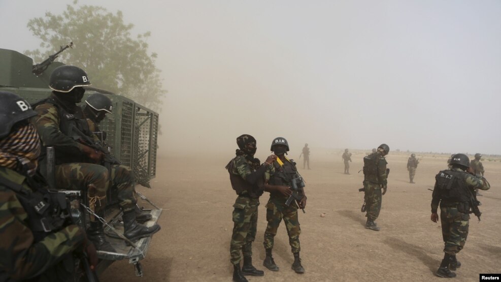 FILE - Cameroonian soldiers from the Rapid Intervention Brigade stand guard amidst dust kicked up by a helicopter in Kolofata, Cameroon, March 16, 2016.