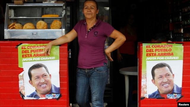 A woman stands in a restaurant between posters of Venezuela's President Hugo Chavez, in front of a military hospital, where Chavez is being treated, in Caracas, February 20, 2013.