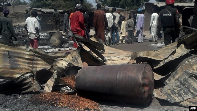 Police officers stand guard in front of the burnt-out remains of homes and businesses in the village of Konduga, in northeastern Nigeria, Feb. 12, 2014.