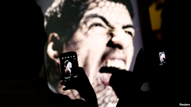 People use mobile devices to take pictures of an advertising placard showing Uruguay's striker Luis Suarez flashing his teeth, Copacabana beach, Rio de Janeiro, June 26, 2014.