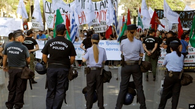 Police officers stand in front of the protesters during an anti-bailout protest outside of the Cyprus parliament in Nicosia, April 30, 2013.