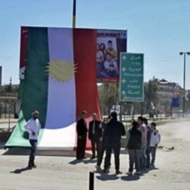 People stand in front of a Kurdish flag during a protest against Syria's President Bashar al-Assad and a celebration of Nowruz held by Qamishli's Kurdish community, March 21, 2012.