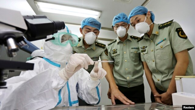 FILE - A health inspection and quarantine researcher, left, demonstrates to customs policemen the symptoms of Ebola, at a laboratory at an airport in Qingdao, Shandong province, Aug. 11, 2014.  