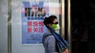 A woman wears a face mask as she walks past a poster showing how to avoid the H7N9 avian influenza virus, by a road in Beijing, April 24, 2013.