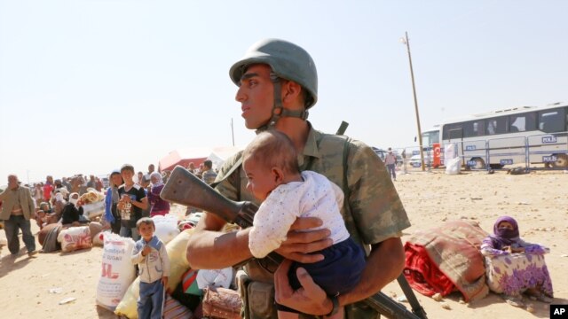 Một binh sĩ Thổ Nhĩ Kỳ bế một em bé bị lạc trong khi đi tìm bà mẹ. Hàng ngàn ngượi tị nạn chạy từ thị trấn Kobani đến cửa khẩu biên giới Syria-Thổ Nhĩ Kỳ, 2/10/14