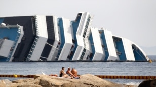 June 20, 2012: Vacationers bask in front of the wreckage of capsized cruise liner Costa Concordia near the harbour of Giglio Porto.