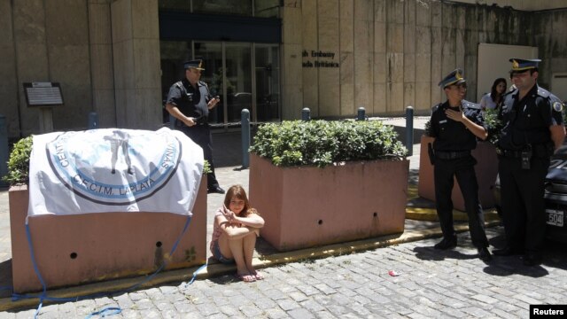 A girl sits beside a sign with the image of a soldier, during a protest by Argentine Falklands War veterans outside the British Embassy in Buenos Aires, January 3, 2013.