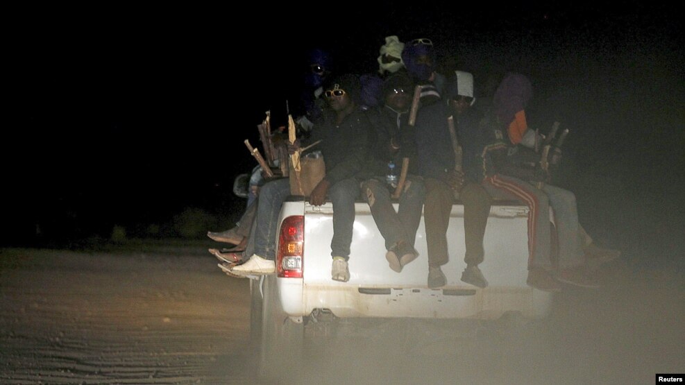 FILE - Migrants sit in the back of a truck as it is driven through a dust road at night in the desert town of Agadez, Niger, May 25, 2015.