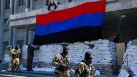 Pro-Russian armed men walk past activists hanging up a "Donetsk Republic" flag outside the mayor's office in Slovyansk, eastern Ukraine, April 21, 2014.