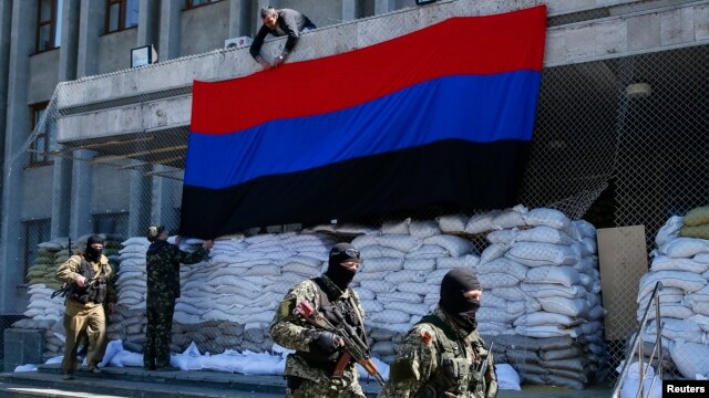 Các tay súng thân Nga đi ngang qua nơi các nhà hoạt động treo cờ 'Cộng hòa Donetsk' bên ngoài văn phòng thị trưởng ở Slovyansk, miền đông Ukraine, ngày 21/4/2014.