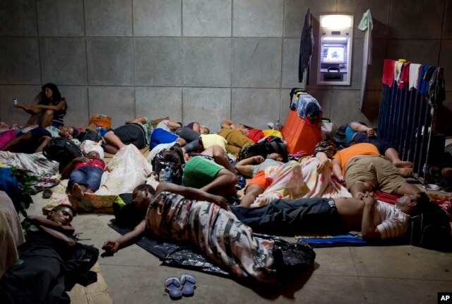 FILE - A Cuban woman migrant uses her cellphone while other Cubans sleep outside the border control building in Penas Blancas, Costa Rica, on the border with Nicaragua, which closed its borders to Cuban migrants, Nov. 21, 2015.