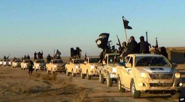FILE - In this undated file photo released by a militant website, which has been verified and is consistent with other AP reporting, militants of the Islamic State group hold up their weapons and wave flags on their vehicles in a convoy on a road leading to Iraq, while riding in Raqqa, Syria.