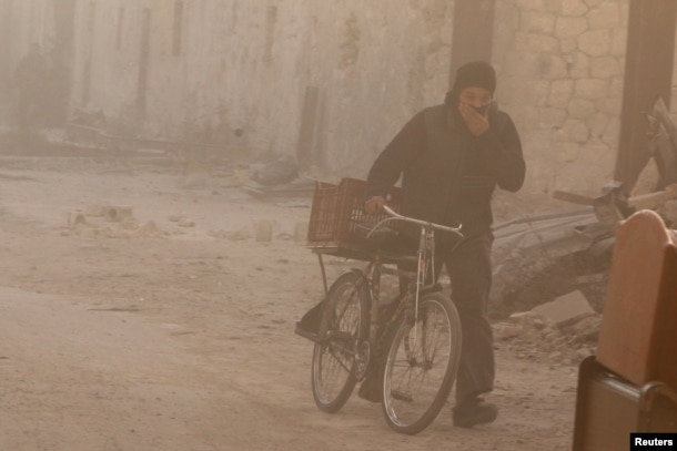 A man covers his face from dust as he walks with a bicycle after a strike on the rebel held besieged al-Shaar neighborhood of Aleppo, Syria, Nov. 26, 2016.