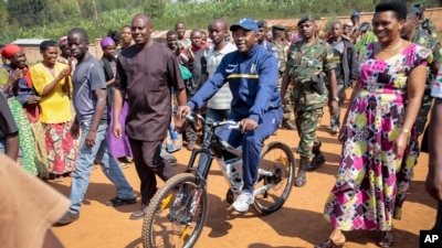 President Pierre Nkurunziza arrives riding a bicycle, accompanied by first lady Denise Bucumi Nkurunziza, right, to cast his vote for the presidential election, in Ngozi, Burundi, July 21, 2015.