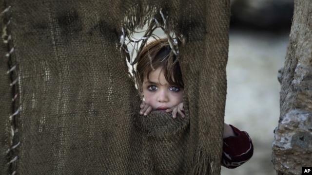 A Pakistani child, who was displaced with her family from Pakistan's tribal areas, looks out through a hole of a makeshift curtain at the entrance of her family's home, in a poor neighborhood on the outskirts of Islamabad, Pakistan, Monday, Jan. 28, 2013.