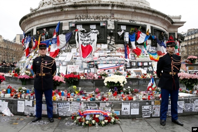 French honor guards stand next to the monument at Place de la Republique in Paris, where people laid candles cards and flags during a ceremony to honor the victims of the Islamic extremist attacks, Jan. 10, 2016.