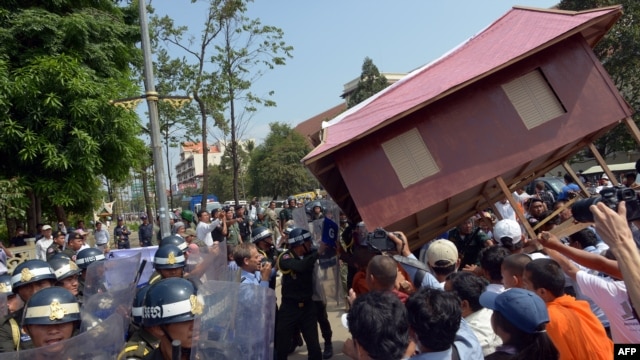 People carry a giant model of a house toward police as they protest government-sanctioned evictions, World Habitat Day, Phnom Penh, Oct. 10, 2013.