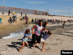 Una familia de migrantes, parte de la caravana de miles que viaja desde Centroamérica hacia Estados Unidos, corre para escapar del gas lacrimógeno en la frontera entre Estados Unidos y México en Tijuana, el 25 de noviembre del 2018.