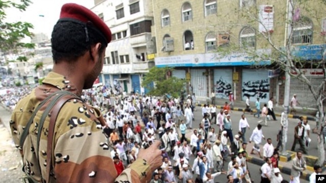 Army soldier watches as anti-government protesters march during a demonstration demanding the ouster of Yemen's President Ali Abdullah Saleh in the southern city of Taiz, April 26, 2011