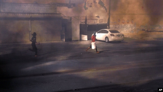 Masked Bahraini anti-government protesters run through smoke after setting tires alight on a road in the village of Dumistan, January 7, 2013.