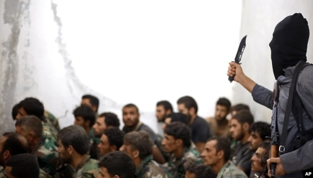 FILE - This undated file photo posted on Wednesday, Aug. 27, 2014 by the Raqqa Media Center of the Islamic State group, a Syrian opposition group, which has been verified and is consistent with other AP reporting, shows a fighter from the Islamic State group with Syrian prisoners.