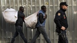 Immigrant street vendors in Spain walk along carrying their goods as police stand guard in Madrid, Spain