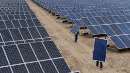 FILE - Employees carry solar panels at a solar power plant in Aksu, Xinjiang Uyghur Autonomous Region, May 18, 2012.