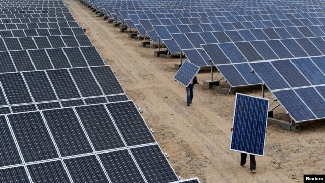 FILE - Employees carry solar panels at a solar power plant in Aksu, Xinjiang Uyghur Autonomous Region, May 18, 2012.