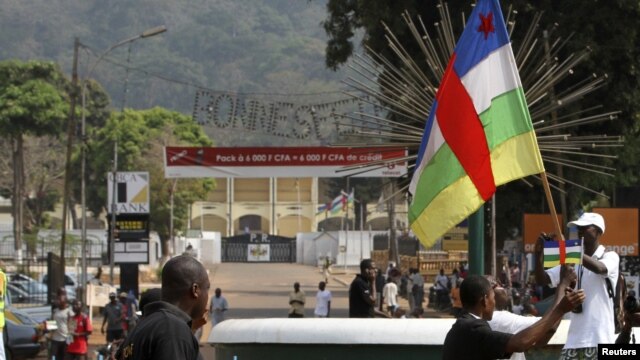 A man holds a flag during a demonstration near the presidential palace, seen in the background, in Bangui, Central African Republic, Jan. 5, 2013.