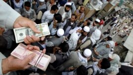An Afghan trader holds U.S. dollar and Afghani bundles at the Saray- e Shahzadeh, the main exchange market in Kabul, Afghanistan, Sept. 18, 2011.