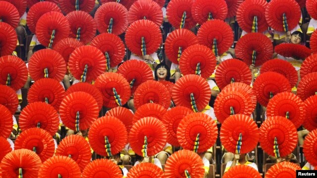 A girl laughs as she sits among hand fans during a mass performance at a children's martial arts fair in Foshan, Guangdong province, May 31, 2013. 