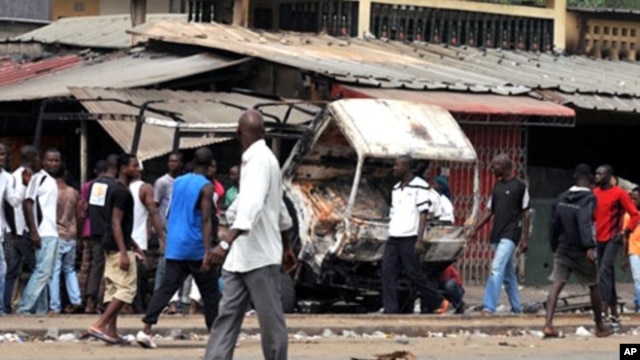 Residents look at a vehicle of FDS - troops loyal to incumbent president Laurent Gbagbo - burned in the Abobo district of Abidjan, 12 Jan 2011