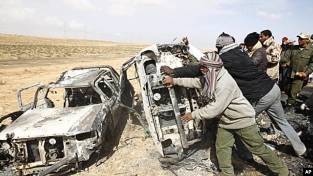 Rebel fighters push cars burnt in what they say was a coalition airstrike on a group of vehicles killing around ten on the road between Ajdabiyah and Brega, in Libya, April 2, 2011