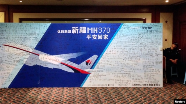 Cảnh sát ngồi ngủ cạnh tấm bảng ghi các thông điệp cho hành khách của chuyến bay MH370 bị mất tích tại Lido Hotel ở Bắc Kinh.