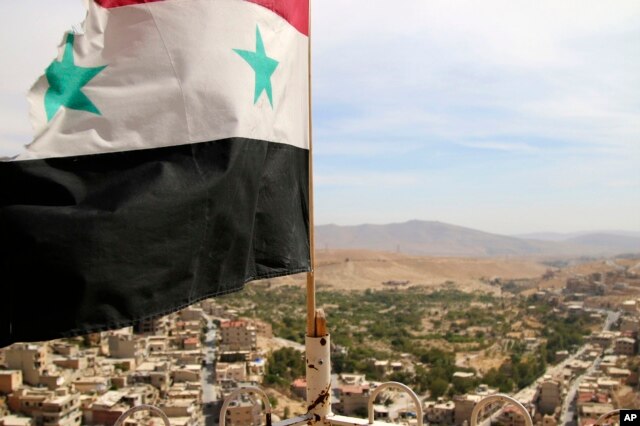 In this photo taken on Sunday, Oct. 18, 2015, a Syrian flag flies above the village of Maaloula, north of Damascus, Syria.