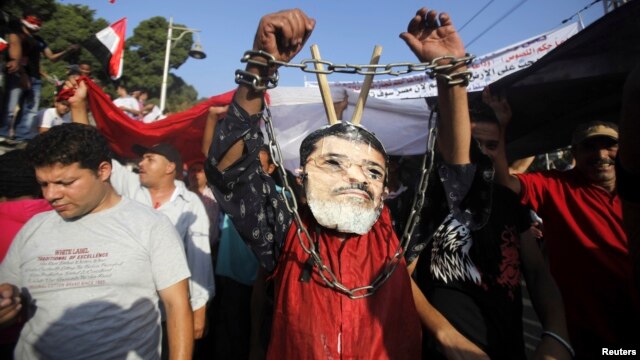 Seorang demonstran anti Presiden Mohamed Morsi mengenakan topeng Morsi dengan tangan yang dirantai dalam protes di depan Istana Presiden di Kairo (30/6). 
