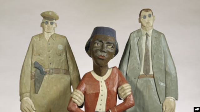 In this wooden sculpture by Marshall D. Rumbaugh, Rosa Parks is held by two policemen.  Parks was arrested after refusing to give up her seat to a white male bus rider in Montgomery, Alabama.