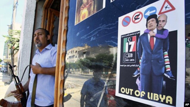 A Libyan rebel stands by a shop window decorated with a portrait of Moammar Gadhafi with his son Seif al-Islam on his shoulders, in Tripoli, Aug. 25, 2011