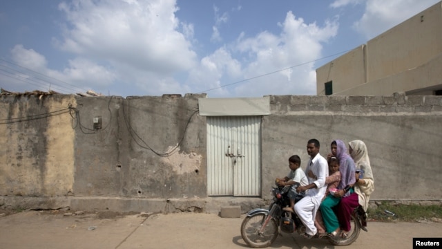 A family rides past the locked house of Rimsha Masih, a Pakistani Christian girl accused of blasphemy, on the outskirts of Islamabad, August 23, 2012.
