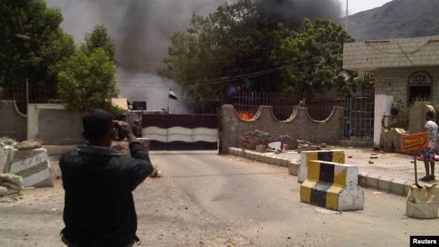A man takes a photo of smoke rising from the site of an attack on the Political Security Agency building, the headquarters of the Yemeni intelligence services in the southern provinces, in the southern Yemeni city of Aden August 18, 2012. 