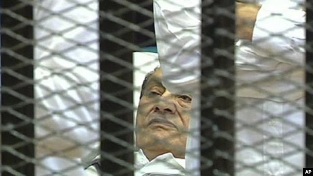 This video image taken from Egyptian State Television showing former Egyptian president Hosni Mubarak laying on a hospital bed flanked by his two sons Gamal and Alaa, inside a cage of mesh and iron bars in a Cairo courtroom, Wednesday Aug. 3, 2011,  as hi