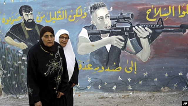 Palestinian women walk next to a mural of militants on the first day of Eid al-Fitr in the West Bank town of Jenin, August, 30, 2011.