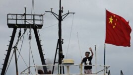 Captain Why Yang of Hong Kong fishing vessel "Kai Fung No.2" waves next to a Chinese national flag as he reaches in Hong Kong's island of Cheung Chau, August 22, 2012. 