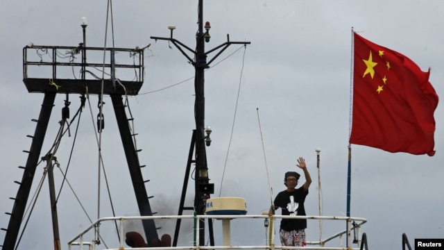 Captain Why Yang of Hong Kong fishing vessel "Kai Fung No.2" waves next to a Chinese national flag as he reaches in Hong Kong's island of Cheung Chau, August 22, 2012. 