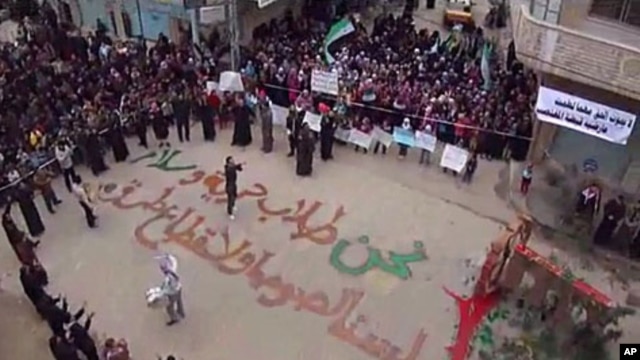 In this image from amateur video made available by the Shaam News Network and shot on Friday, December 30, 2011, protesters gather in Homs, Syria. The writing on the ground, in Arabic, reads: "We are those who seek freedom and peace. We are not thieves or