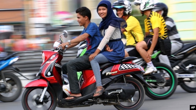 Một phụ nữ ngồi (dạng chân) trên xe gắn máy chạy trên một con đường trong tỉnh Aceh, Indonesia