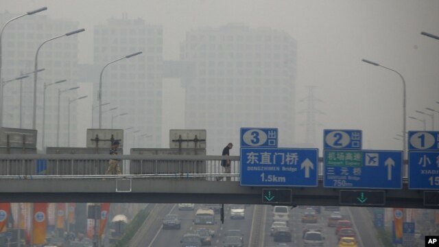 A pedestrian walks across a bridge above a main road on a day with high air pollution in Beijing, June 6, 2012.