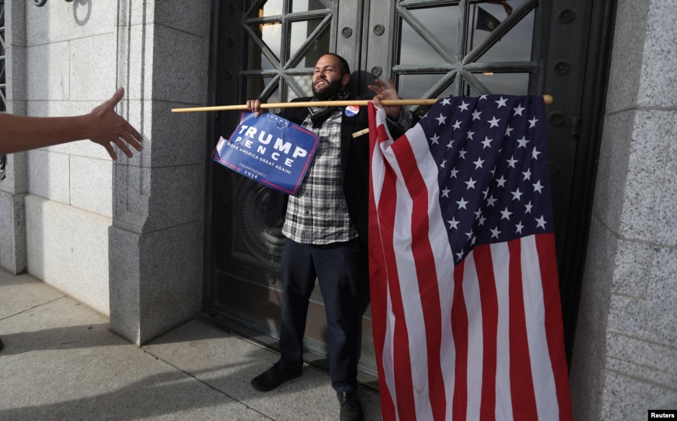 在鹽湖城，麵對反川普示威，有擁護川普者站在猶他州議會門前，手持國旗和標語&ldquo;川普 彭斯&rdquo;（2016年11月12日）