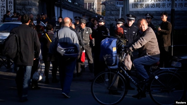 A man cycles past security personnel, and uniformed and plainclothes police, who are standing outside the entrance to a government building where petitioners congregate daily to protest private equity scams, in central Beijing, October 22, 2012.
